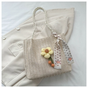 Détail du sac cabas en paille tressée avec fleur jaune et foulard décoratif