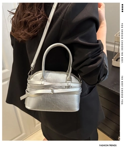 Detail of silver shell-shaped bag with metallic finish and buckle straps shown on model