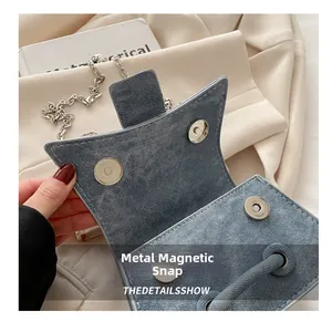 Close-up of the silver magnetic snap closure on a light blue denim textured handbag