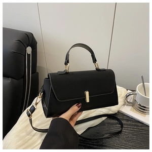 Detail of black faux leather bag featuring glossy gold clasp and detachable shoulder strap