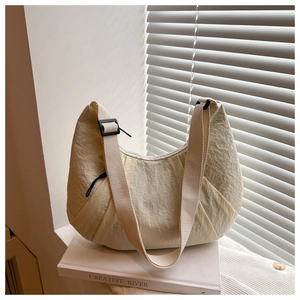 Détail du sac beige en nylon plissé avec bandoulière large sur un livre blanc