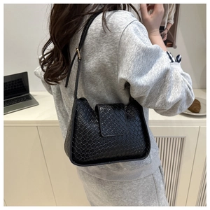 Détail d'un sac à épaule en cuir tressé noir avec fermeture à rabat et bandoulière réglable