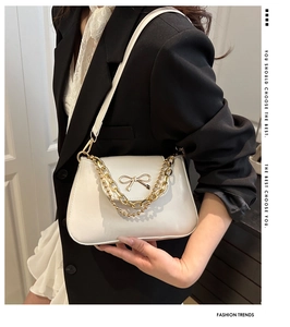 Close-up of white shoulder bag featuring a gold bow and elegant double metal chains