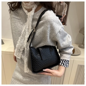 Détail d'un sac hobo noir tressé porté par un mannequin montrant taille et texture