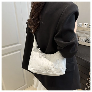 Détail de la broderie de dentelle sur un sac bandoulière beige avec blazer noir