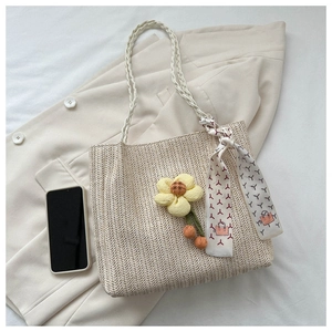Détail du sac seau en paille tressée avec breloque fleur et poignée foulard en soie