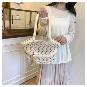 Detail of hand-woven straw tote bag with brown embroidery and decorative fringe tassel