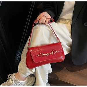Close-up of red patent leather shoulder bag featuring a gold horsebit metal buckle