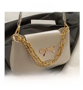 Close-up of cream baguette bag with gold bow clasp and decorative double chains