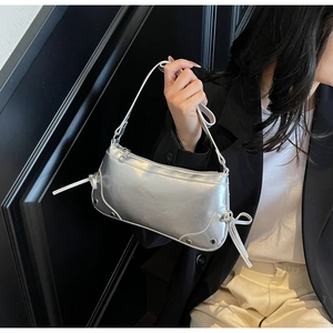 Detail of silver metallic shoulder bag with bow knot and rivet accents on wrinkled leather