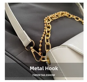 Macro shot of gold-plated lobster clasp and metal chain details on a white leather bag