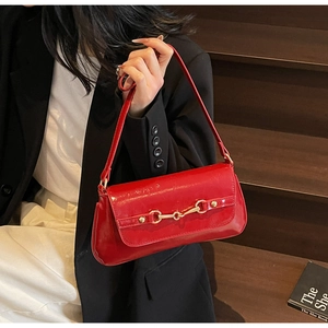 Detail of red patent leather shoulder bag featuring a gold horsebit buckle and sleek strap