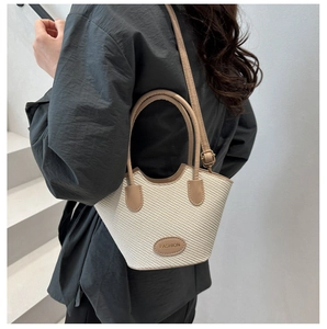 Detail of woven bucket bag featuring contrast leather trim and adjustable shoulder strap