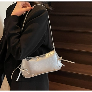 Detail view of silver metallic underarm bag with decorative bow ties and rivets