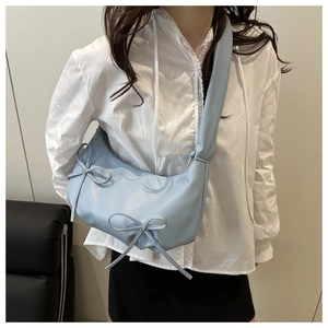 Detail of light blue shoulder bag with bow decor and wide strap on model