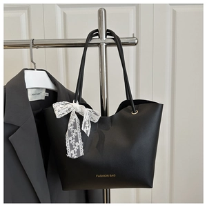 Détail d'un sac cabas en cuir noir avec lettrage doré et nœud en dentelle blanche