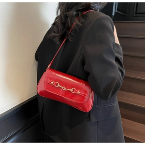 Detail of red glossy baguette bag with gold horsebit hardware worn over the shoulder