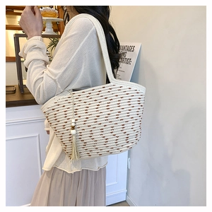 Close-up of beige woven tote bag with fringe tassel and horizontal striped texture details