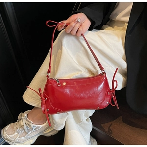 Detail of red patent leather shoulder bag featuring bow ties and silver metal studs