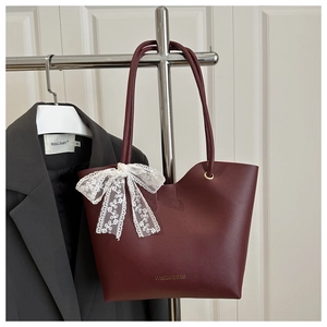 Détail du sac cabas en cuir bordeaux avec nœud en dentelle blanche et texte imprimé