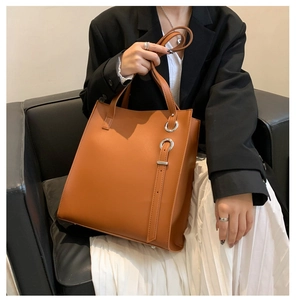 Brown faux leather tote bag with silver ring detail worn by a model in office attire