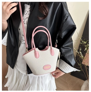 Detail of pink and beige woven crossbody bag worn with a black jacket and white skirt