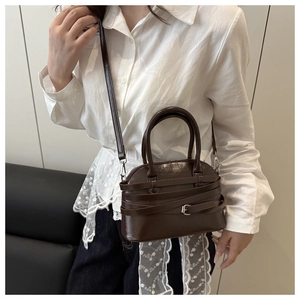 Brown glossy handbag with triple strap buckle design shown in a cross-body wear scene