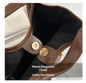 Detail of golden magnetic buckle closure and black lining on brown textured tote bag