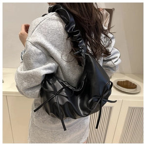 Close-up of black hobo bag with pleated shoulder strap and bow details on a model