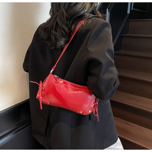 Detail of red patent leather baguette bag with side bow and silver rivets on the shoulder strap