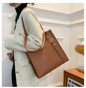 Detail of caramel leather tote bag showing side silver metal ring and sleek square shape