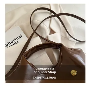 Detail of vintage brown leather bag featuring golden cat paw emblem and sleek shoulder strap
