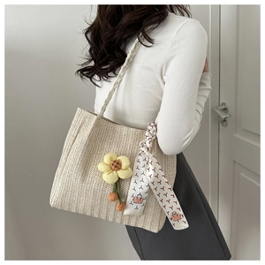 Détail du sac seau en paille tissée avec charm floral et accent de foulard en soie
