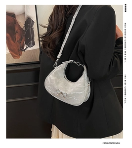 Silver metallic pleated crescent bag with bow detail worn by a model in a black suit