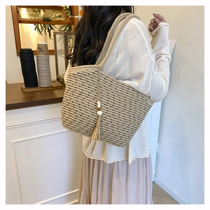 Detail of woven straw shoulder bag with tassel charm and wooden beads on model