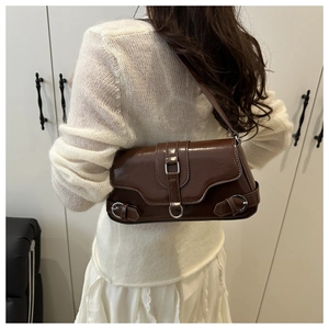 Sac à bandoulière marron en cuir synthétique avec boucles argentées porté par un modèle