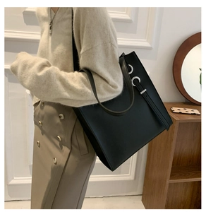 Detail of minimalist black tote bag featuring silver eyelet hardware and thin strap detail
