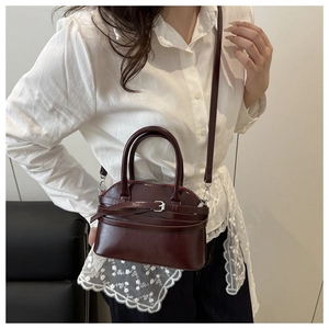 Deep red glossy leather semi-round handbag carried by model for a commute look