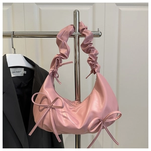 Close-up of pink pleated shoulder bag with decorative bows and crescent moon shape
