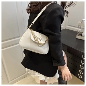 Detail of cream white underarm bag with gold chain and bow decoration on the flap