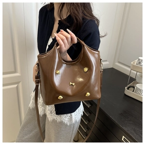 Detail of brown tote bag featuring gold dog-themed metal rivets and detachable shoulder strap