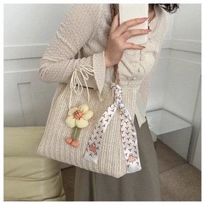 Gros plan d'un sac seau tressé beige avec breloque florale et foulard en soie élégant