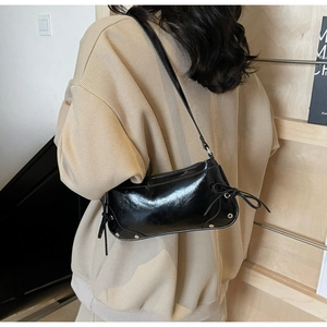 Details der schwarzen glänzenden Schultertasche mit Knotenschleife und Nieten