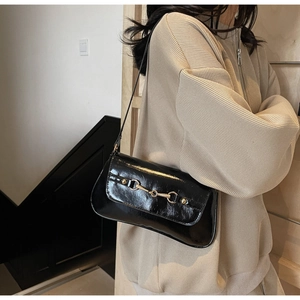 Detail of black patent leather underarm bag with gold horsebit and sleek shoulder strap