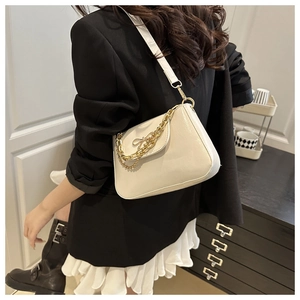 Detail of cream white underarm bag with gold bow clasp and metal chain on a model