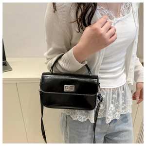 Petit sac carré en cuir brillant noir avec fermoir rotatif porté par un mannequin