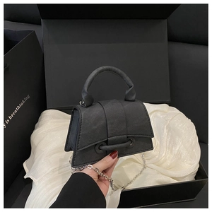 Detail of a black textured fabric hourglass handbag with silver chain in a gift box
