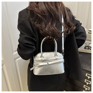 Detail of silver metallic handbag with unique cross-strap design held by a model