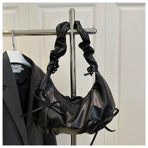 Detail of ruched shoulder strap and bow decoration on black PU leather underarm bag