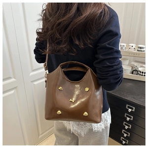 Detail of glossy brown tote bag featuring golden puppy and bone metal charms